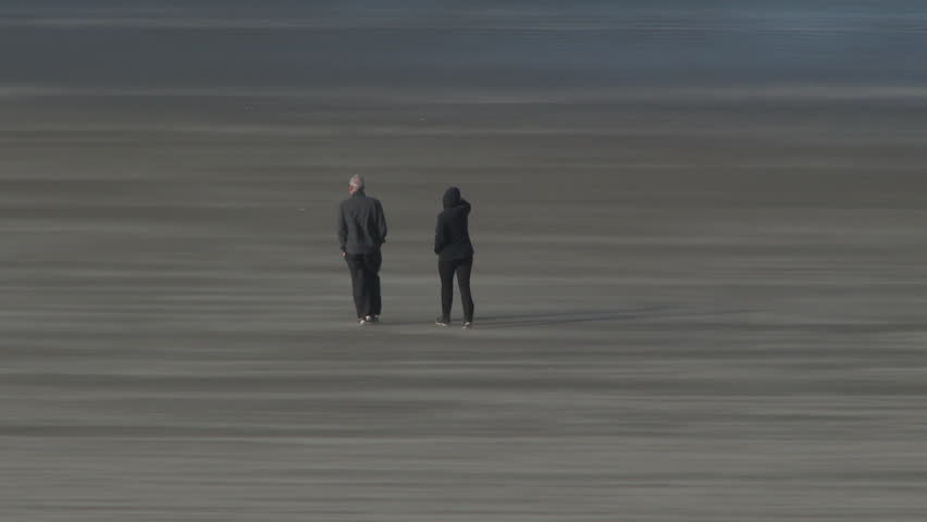 Couple walking on sandy beach in Oregon during heavy wind storm.