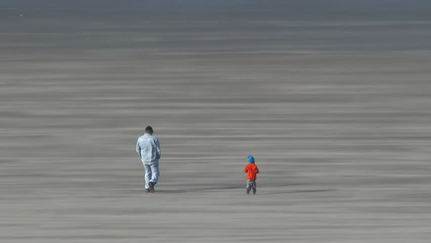 Father and son walking on sandy beach in Seaside, Oregon on extremely windy day.