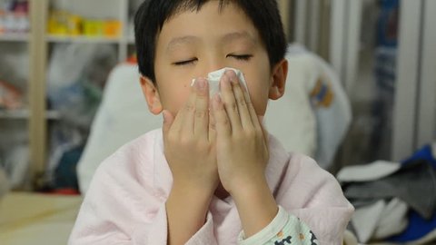 Young Asian boy blows his nose using toilet paper