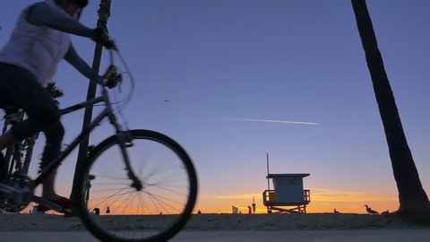 Bicyclists cycle in front of sunset as silhouettes between Santa Monica and Venice Beach in Los Angeles, California. Slow motion. Stock Video