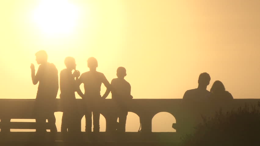 Silhouetted group of boys hanging out on promenade with cute, loving couple on sunny day in Seaside, Oregon.