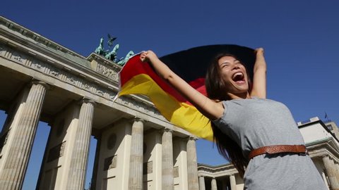 German flag - Woman happy at Berlin Brandenburger Tor cheering celebrating waving flag by Berlin Brandenburg Gate, Germany. Cheerful excited multiracial woman in Germany travel concept.
