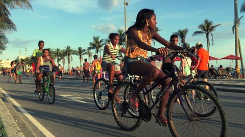 RIO DE JANEIRO, BRAZIL - JANUARY 25, 2015: Young Brazilians pass by on bicicyles in slow motion on a car-free Sunday on the beachfront road Avenida Vieira Souto. Editorial Stock Video