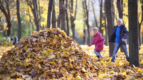 Boy and girl jump to big heap of yellow fallen leaves in autumn park