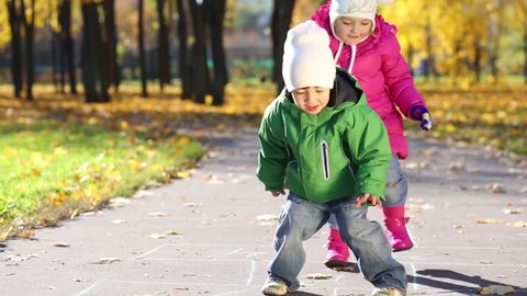Two children play hopscotch in autumn park with dry leaves