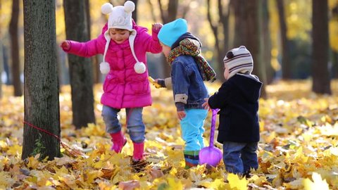 Three happy children play in autumn park with dry yellow leaves