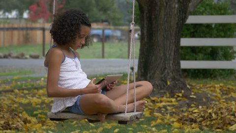 Young Girl on a Swing Holding a Tablet Horizontal Medium Shot