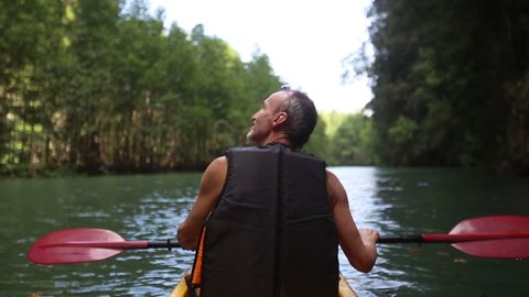 elderly man swim down the river on kayak looks around and points by his finger