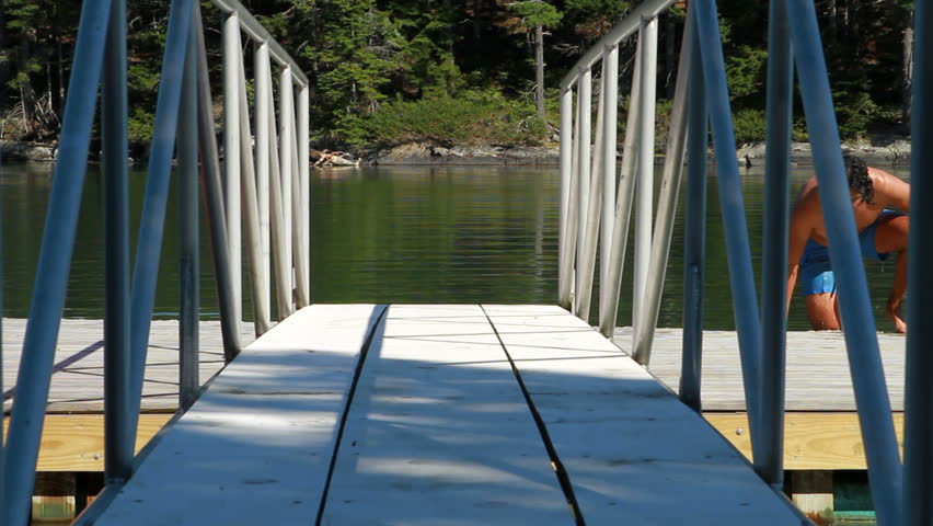 A man sits at the edge of a dock after swimming.