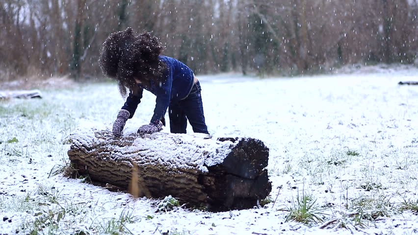 Little child gathering snow from a fallen tree as it snows around her