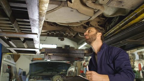 Mechanic inspects the car undercarriage way and makes a note on his inspection sheet