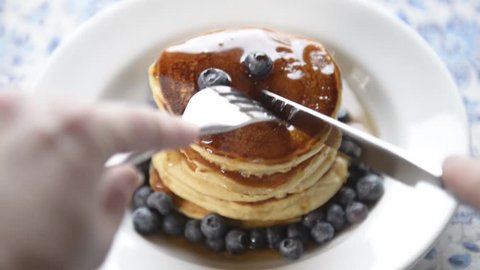 Woman eats delicious hot pancakes with fresh blueberries and natural maple syrup