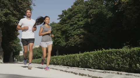 Sport couple running jogging in city park. Runners exercising - woman and man runner training on run living healthy active lifestyle in Retiro Park in Madrid, Spain, Europe. RED EPIC SLOW MOTION.