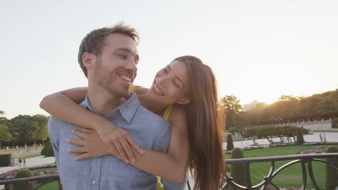 Romantic couple embracing in love laughing having fun. Multicultural man and woman smiling happy in el Retiro in Madrid, Spain, Europe. Asian girl, young Caucasian man. RED EPIC SLOW MOTION.