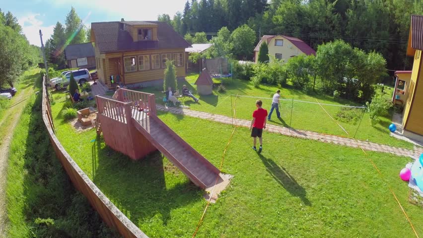 Ten members family get rest and play badminton on yard in cottage settlement at summer day. Aerial view