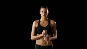 Young athletic woman wearing sporstwear is drinking water from plastic bottle - isolated-on-black HD video footage