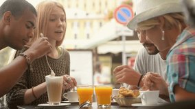 Four multiethnic friends have breakfast eating jam stuffed brioches and drinking cappuccino or orange juice in summer day - HD video footage