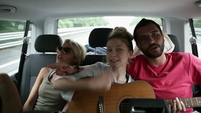 Three young friends have fun singing with guitar during a travel in a moving van - HD video footage