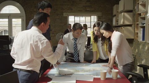 4K Asian business team in strategy meeting, looking at a map of the world