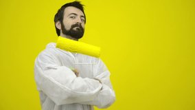 Young satisfy man gesturing with a yellow paint roller in front of a yellow painted wall - HD video footage