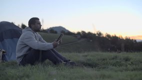 Young man using tablet in nature mountain outdoor at sunrise or sunset - dolly HD video footage