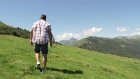 Back view of young man hiking in mountain outdoor nature scenery during sunny summer day - gimbal steadicam HD video footage