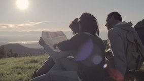 Young friends doing camping looks at map in mountain outdoor nature scenery during summer sunrise or sunset - HD video footage