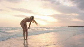 Young woman plays with water at sunrise or sunset on ocean beach sea-side in summer - gimbal steadicam HD video footage