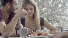 Couple of happy man and woman friends smile, laugh and drink coffee during italian breakfast on a summer sunny day morning in tuscany, italy - slow-motion HD video footage