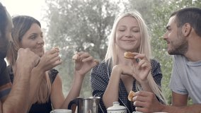 Group of four happy men and women friends smile, laugh, eat croissants during italian breakfast on a summer sunny day morning in tuscany, italy - slow-motion HD video footage