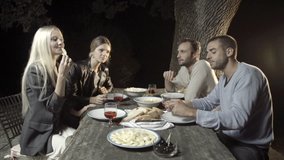 Group of four happy men and women friends smile and enjoy aperitif in outdoor rural scenic at night - slow-motion HD video footage