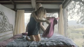 Two young women, friends or homosexual lesbian couple, do a pillow fight on bed in the morning - slow-motion HD video footage