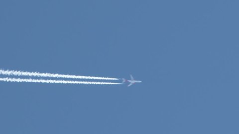 4K - Airplane flies overhead through frame on clear, blue sky day leaving behind vapor trail jet contrails.