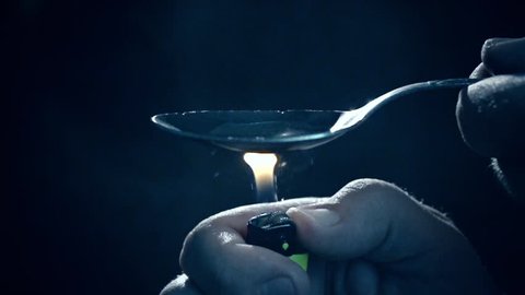 Man's hand sets fire the lighter over spoon of boiling drug, diluted heroin. Slow Motion. Social degradation, self-destruction of narcomaniac junkie.