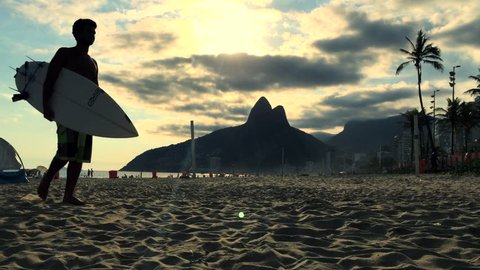 Sunset silhouette of young Carioca Brazilian surfer walking with surfboard on Ipanema Beach Rio de Janeiro Brazil