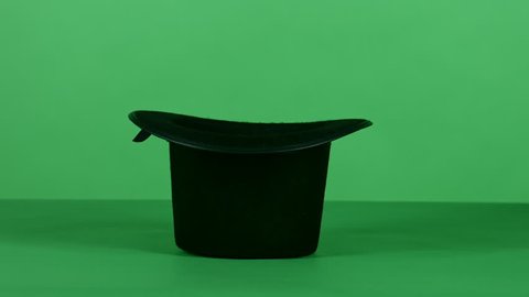 A magician does the tick with an empty black top hat and a magic wand in front of a green screen background