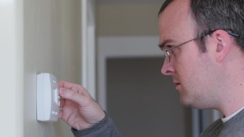 A man changing the temperature on a programmable thermostat on the house wall