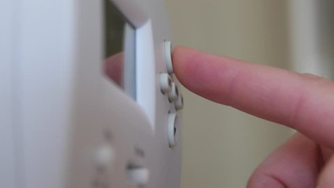 A man changing the temperature on a programmable thermostat on the house wall