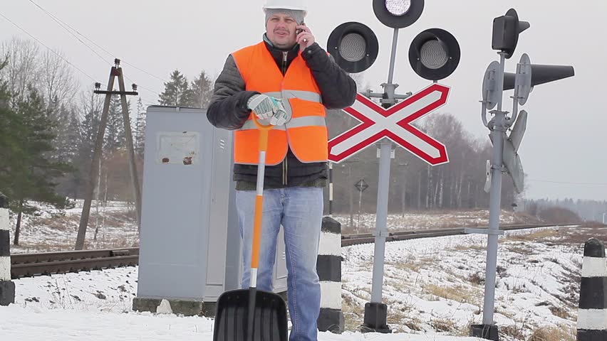 Man with cell phone and snow shovel on a railway crossing