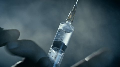 Man flicks syringe prior to drug injection, to collect and release the air out of the syringe. Heroin or meth. Smoke background. Social degradation, self-destruction of narcomaniac junkie.