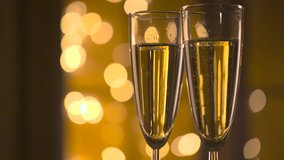 Champagne Pouring from the bottle. Two Flutes with Sparkling Wine over Holiday Bokeh Blinking Background. Couple of champagne Glasses closeup. Success celebrating