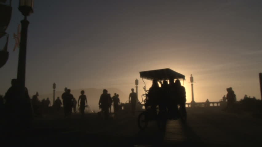 Unrecognizable people silhouetted from sunny day enjoying nice day at beach promenade biking and walking by on boardwalk.