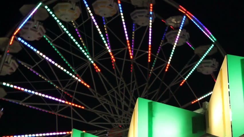 A colorful illuminated ferris wheel turns in the night sky