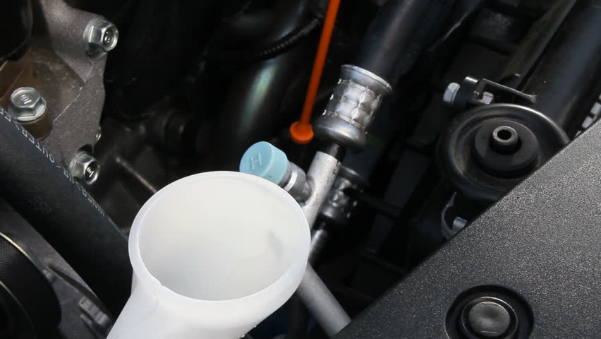 Blue windshield washer fluid is poured into the reservoir to fill it up