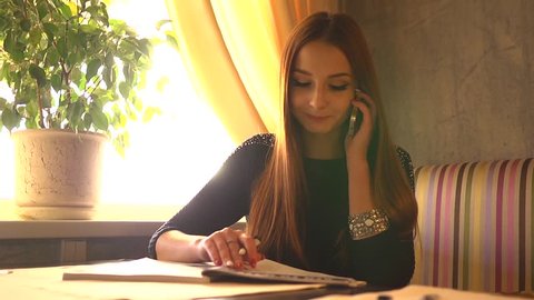 young business woman in a restaurant talking phone and making notes