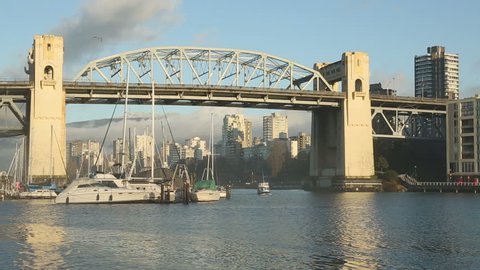 A False Creek Ferry arriving at the Granville Island dock in Vancouver, British Columbia, Canada. The historic Burrard Bridge and the apartments of the West End neighborhood are in the background.