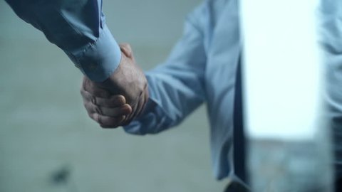 Slow motion of two cropped unrecognizable businessmen shaking hands