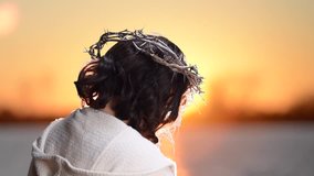 Jesus with crown of thorns view from behind as sun sets