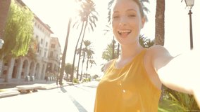 Portrait of attractive young tourist woman visiting a destination city on holiday, holding a video camera and filming herself like in a selfie, networking on vacation. Travel and technology lifestyle.