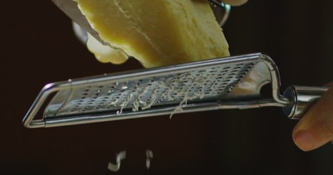 Super slow motion macro of a middle aged chef grating parmigiano-reggiano cheese with steel grater on the dish (close up)